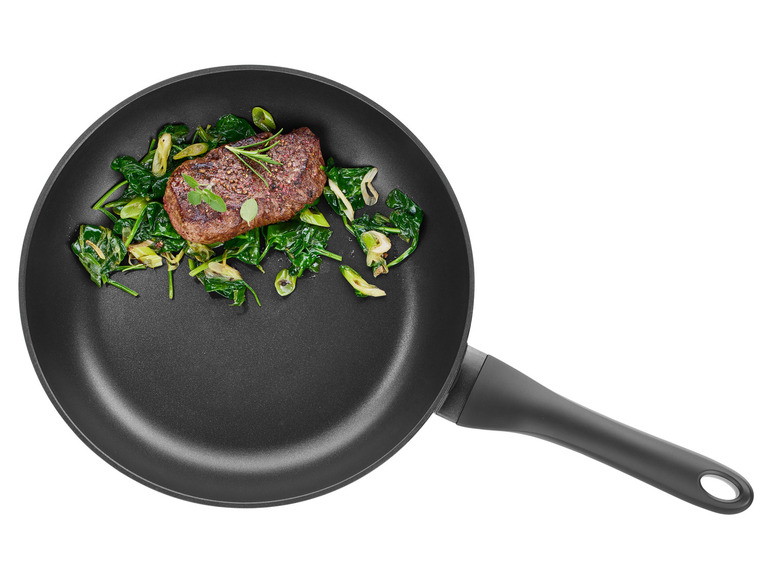 Een gebakken biefstuk met spinazie en bosui in een zwarte koekenpan.