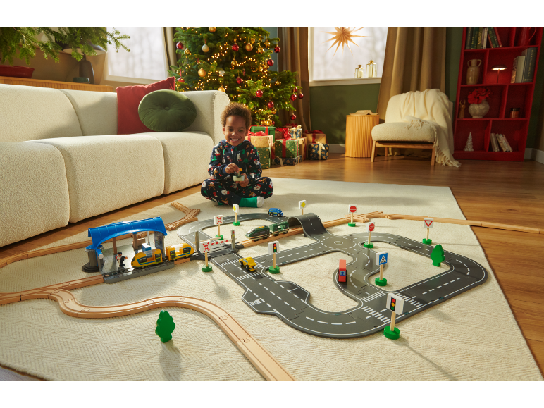 Kind speelt met houten treinset en wegenmat op een vloerkleed in een feestelijke woonkamer.