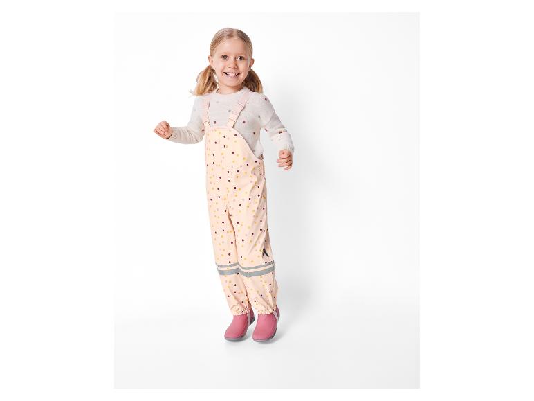 Meisje springt in roze regenbroek en laarzen.