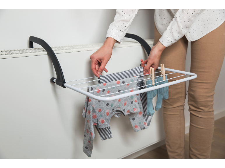 Vrouw hangt babykleding op een droogrek bevestigd aan een radiator.