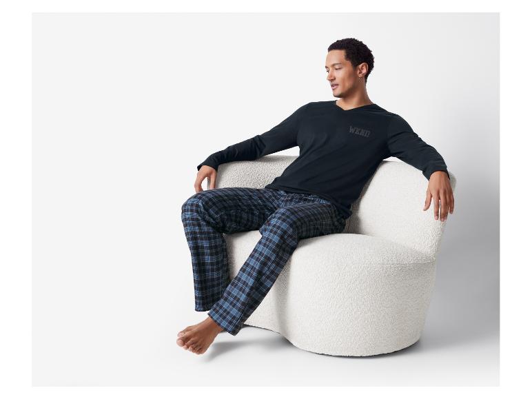 Man in zwart shirt met lange mouwen en blauw geruite pyjamabroek ontspant op een witte stoel.