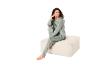 Vrouw in groene pyjama zit glimlachend op een beige poef.