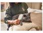 Vrouw borstelt een kat met een witte borstel, de kat is grijs, de vrouw draagt een groene hoodie.
