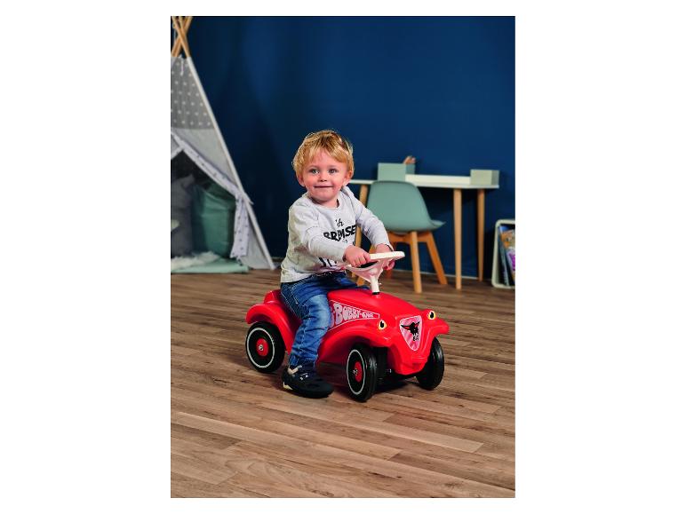 Peuter op een rode loopauto in een kinderkamer.