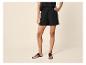 Vrouw in zwarte shorts en platte sandalen, poserend met hand in de zij.