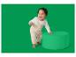 Lachende baby in beige gebreide tuinbroek en witte top, leunend op een groene poef.