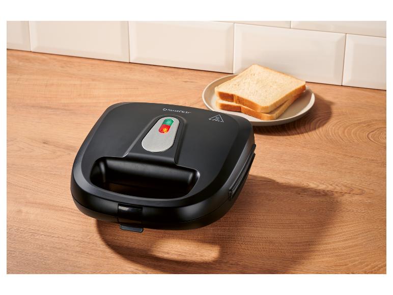 Zwart tosti-apparaat op houten aanrecht met sneetjes brood.