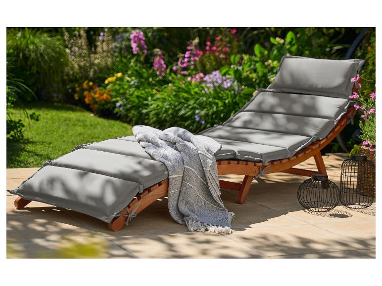 Houten tuinstoel met grijze kussens en een deken op een terras met bloemen.