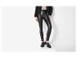 Vrouw in zwarte imitatie leren legging, zwart jasje en zwarte loafers.