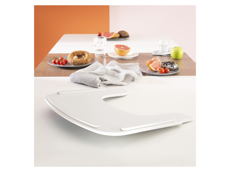 Een wit dienblad met een donut, grapefruit en tomaatjes op een houten tafel.