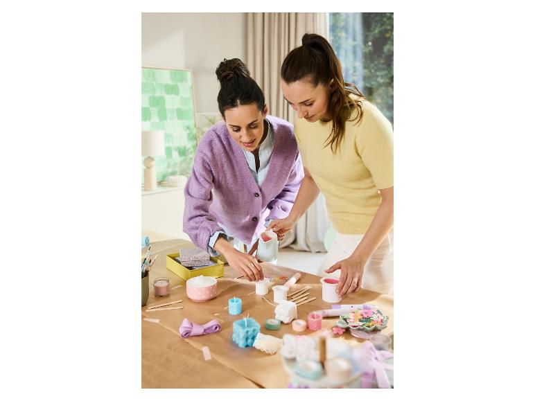Twee vrouwen maken kaarsen en decoraties aan tafel.