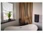 Moderne badkamer met vrijstaand bad, houten lattenwand en groene plant.