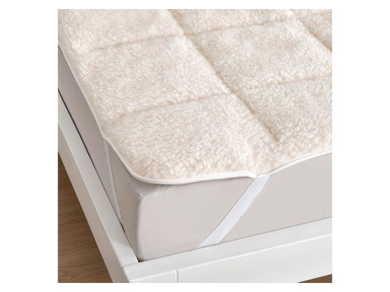 Pluizige, witte matrastopper met elastische banden op een wit bed.