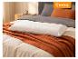 Wit getextureerd kussen op een oranje deken en grijs beddengoed in een slaapkamer