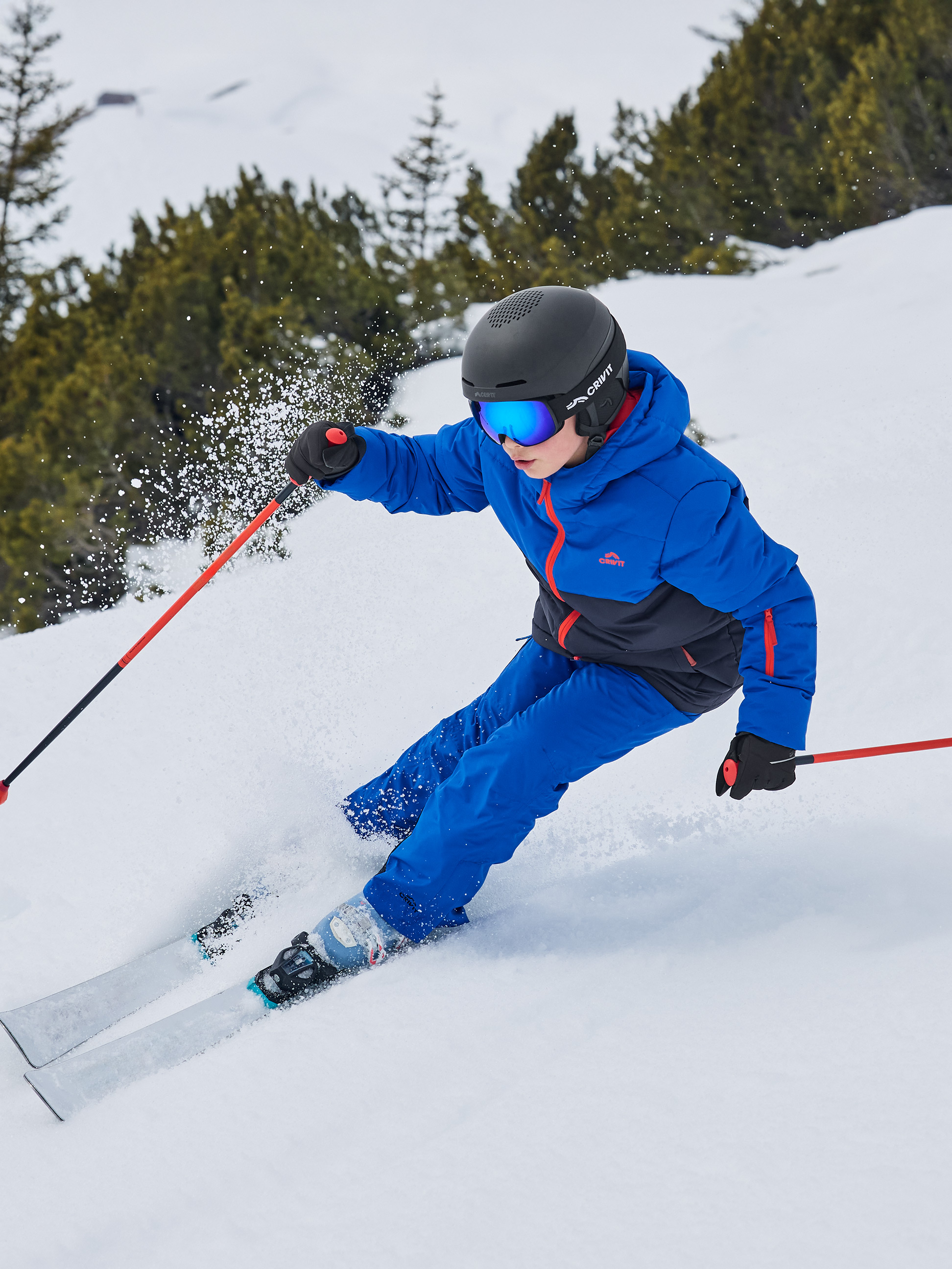 Kind in blauwe ski-jas en -broek, helm en skibril skiet van een besneeuwde helling.