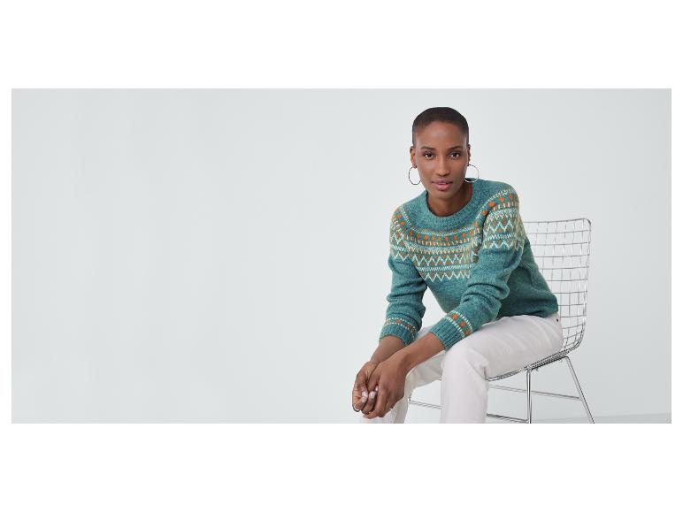 Een vrouw in een groene trui met kerstmotief zit op een stoel.