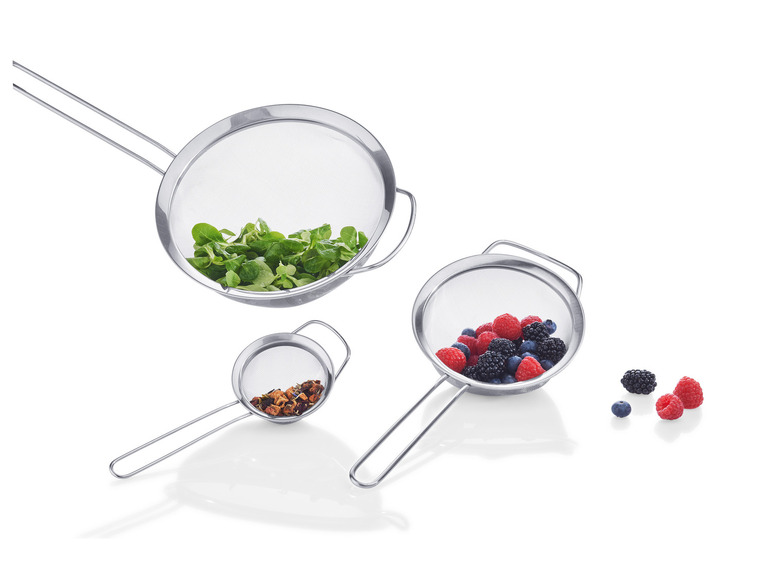 Drie metalen zeefjes met handvatten, gevuld met sla, bessen en thee.