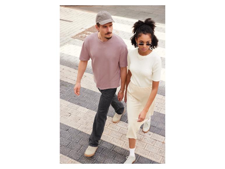 Een man en vrouw lopen op straat, hij draagt een roze t-shirt en zij een witte trui.