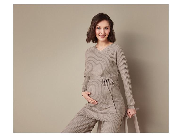 Een zwangere vrouw draagt ​​een beige gebreide trui en broek.