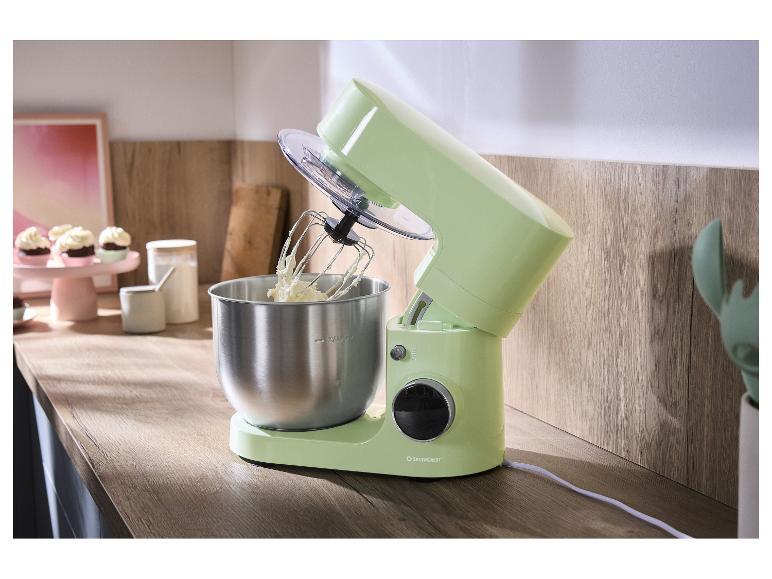 Lichtgroene staande mixer met metalen kom en garde, op een houten aanrecht.