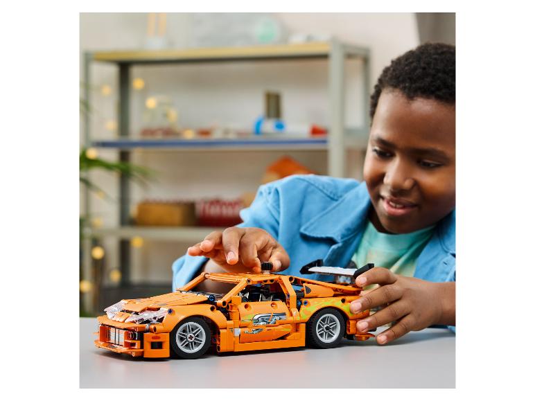 Jongen speelt met een oranje LEGO Technic raceauto op een tafel.