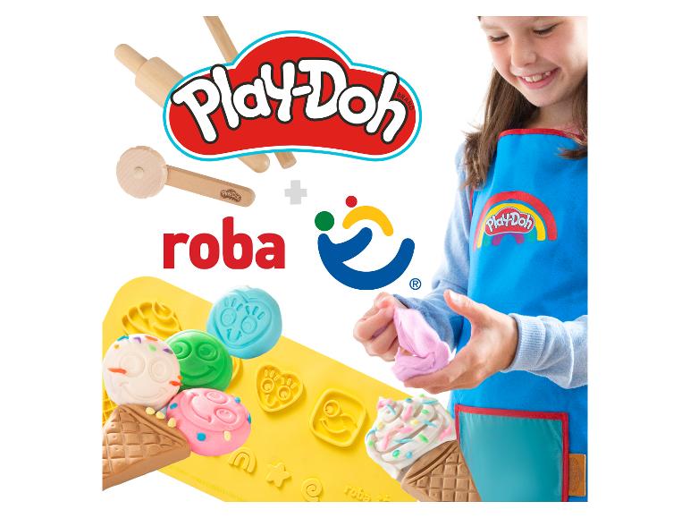 Lachend meisje in blauw schort kneedt roze speeldeeg, met houten gereedschap en siliconen mallen.