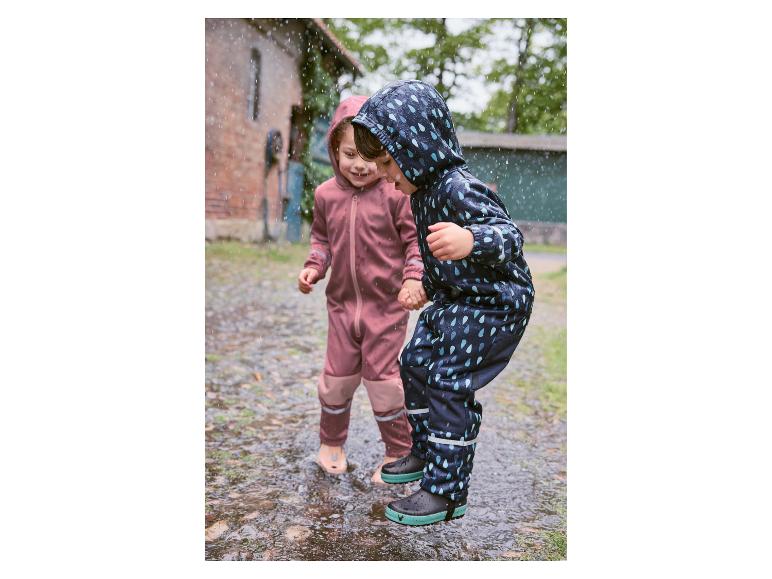 Twee kinderen spelen in plassen met hun regenkleding en laarzen.