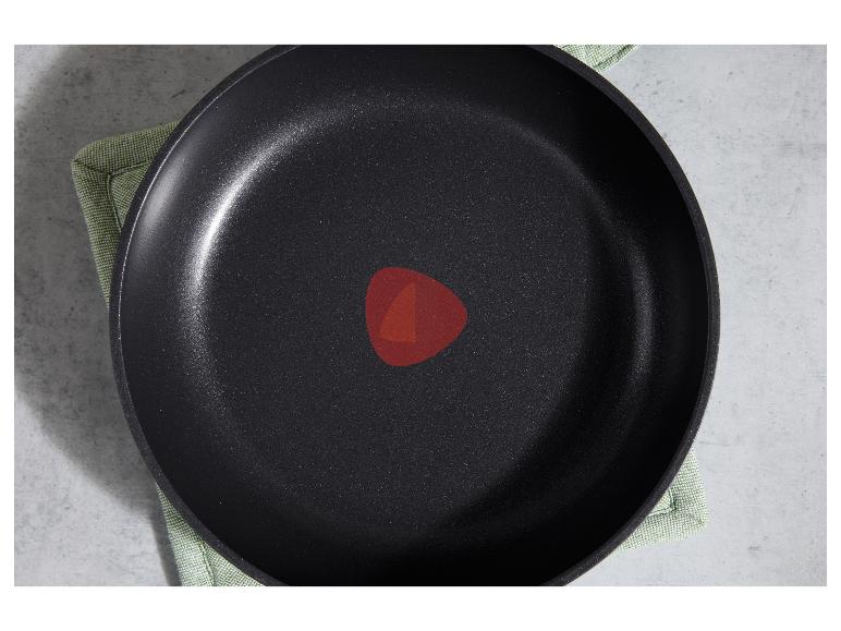 Bovenaanzicht van een zwarte antiaanbakpan met een rode warmte-indicator op een groene doek