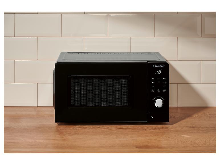 Zwarte magnetron op een houten aanrecht met een betegelde muur op de achtergrond.