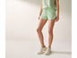 Vrouw draagt groene shorts met witte strepen en witte sneakers.