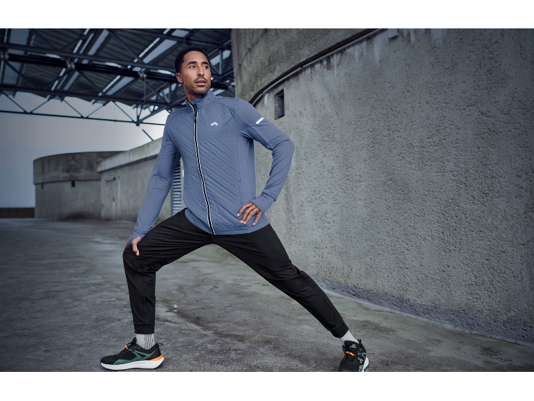 Man in sportjas en -broek die buiten rekt.