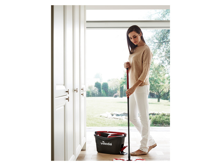 Een vrouw gebruikt een Vileda mop met emmer om de vloer te dweilen.