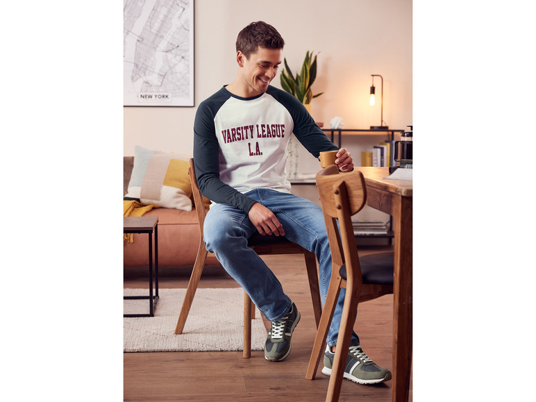 Man in een wit shirt met blauwe jeans en groene sneakers.