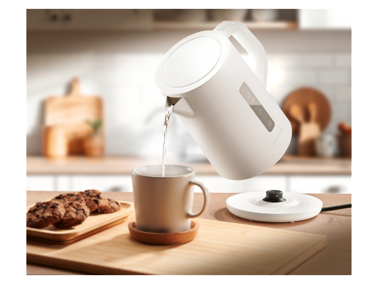 Een witte SilverCrest waterkoker giet water in een mok op een houten tafel.