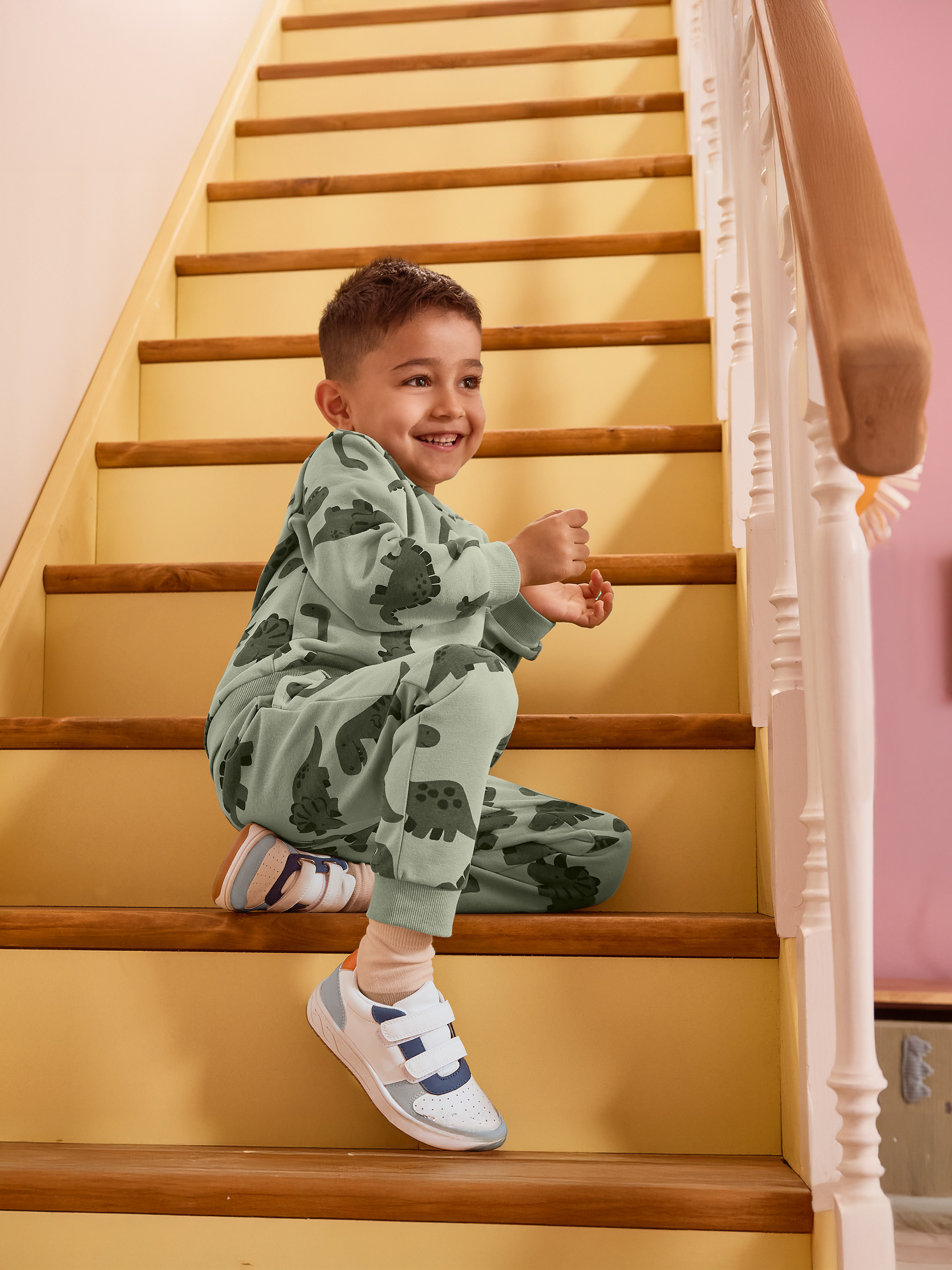 Jongen in groene dinosauruspyjama zit lachend op de trap.