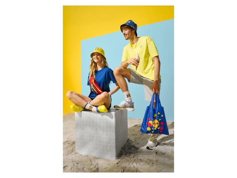 Twee mensen in zomerkleding, hoeden, met een tas en ijsje op een zandachtergrond.