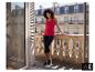 Een glimlachende vrouw in een rode ESMARA® top en zwarte legging op een balkon. [AI-gegenereerde afbeelding]