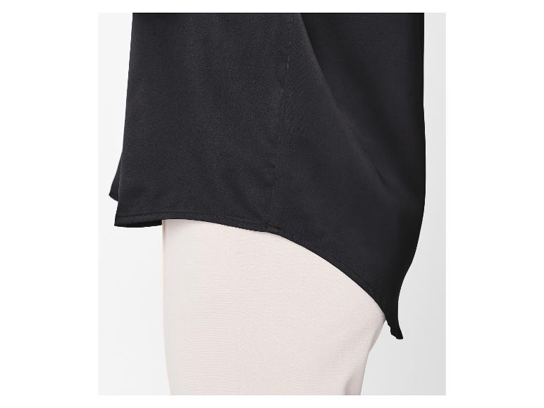 Zwarte blouse met asymmetrische zoom over een lichte broek.