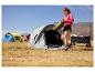 Vrouw met yogamat voor tent, man zet tent op de achtergrond.