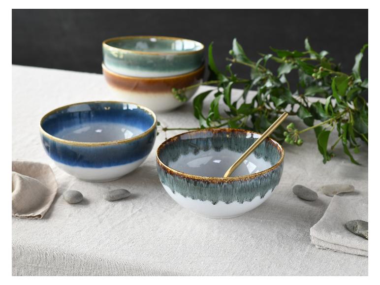 Keramische kommen in blauw, groen en bruin met een gouden rand op een linnen tafelkleed.