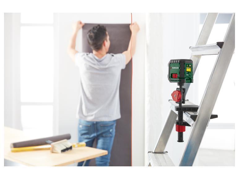 Man gebruikt een Parkside laserwaterpas gemonteerd op een ladder om behang te installeren.