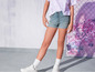 Een meisje draagt blauwe denim shorts, een wit shirt en witte sneakers.