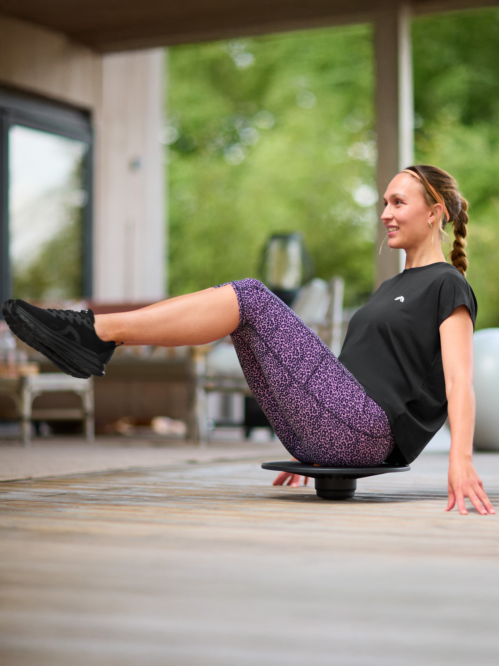 Vrouw traint balans op een balansbord, gekleed in een zwart T-shirt en legging met luipaardprint.