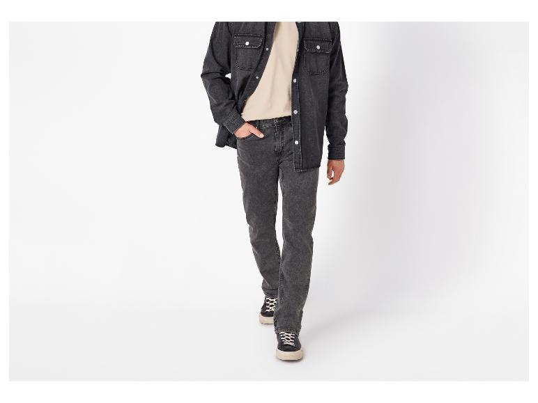 Man in een zwart spijkeroverhemd, beige T-shirt en donkergrijze jeans loopt naar voren.