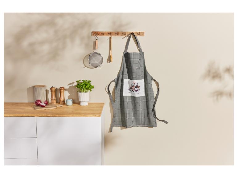 Een geruite keukenschort met een tuinprint hangt aan een wandrek.