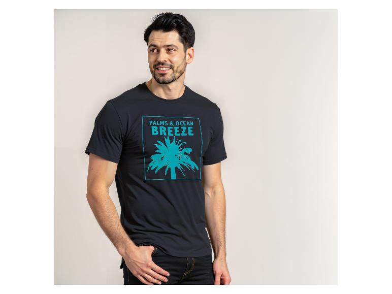 Man in een zwart T-shirt met een turquoise palmboom en de tekst 'PALMS & OCEAN BREEZE'.