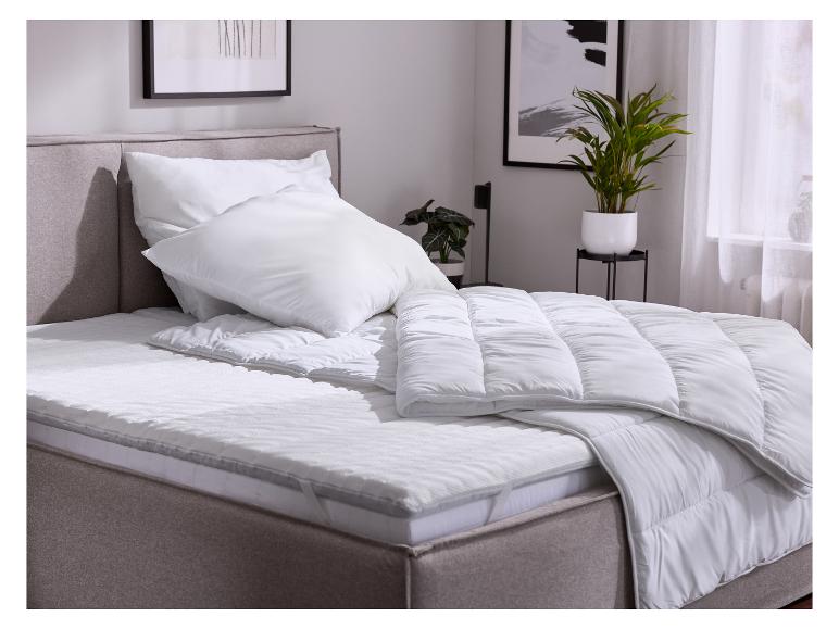 Bed met witte dekbedden, kussens en topmatras in een slaapkamer.