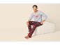 Man zit op een poef, draagt een grijze trui met 'LETS STAY IN BED (FOREVER)' en rood geruite pyjamabroek.