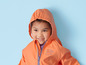 Een kind draagt een oranje regenjas met een capuchon.
