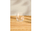 Transparant steeloos glas op een lichte houten tafel met subtiele muurschaduwen.